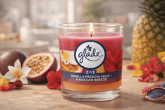 Glade 1-Wick 2in1 scented candle jar with Vanilla Passion Fruit and Hawaiian Breeze fragrance burning on a wooden table surrounded by tropical fruit and flowers
